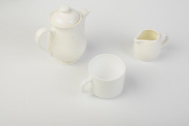 Jarra de leche; taza y tetera de cerámica sobre fondo blanco