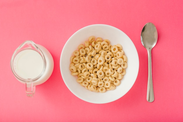 Jarra de leche y tazón de cereales y cuchara sobre el fondo rojo