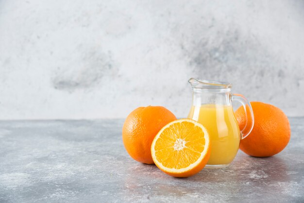 Una jarra de vidrio de jugo con frutas frescas de naranja en la mesa de piedra.