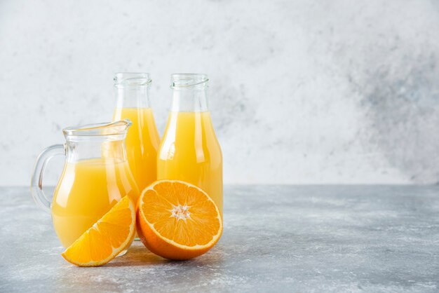 Una jarra de vidrio de jugo con frutas frescas de naranja en la mesa de piedra.