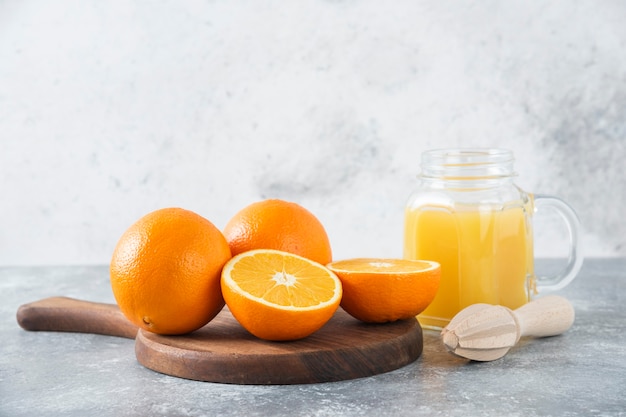 Una jarra de vidrio de jugo con frutas frescas de naranja en la mesa de piedra.