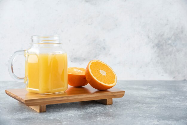 Una jarra de vidrio de jugo con frutas frescas de naranja en la mesa de piedra.