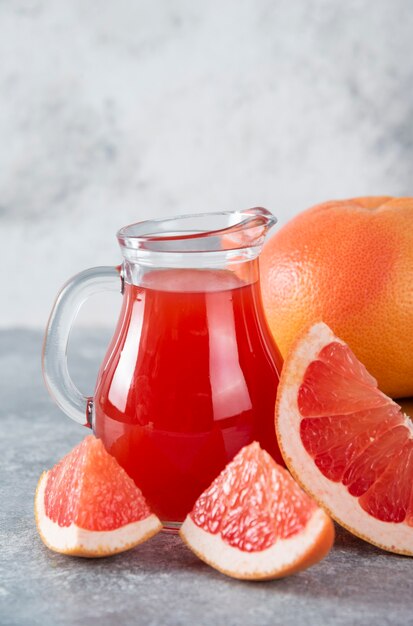 Jarra de vidrio de jugo de pomelo fresco con rodajas de frutas.