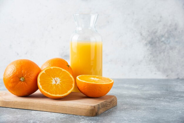 Jarra de vidrio de jugo con rodajas de naranja sobre una tabla de madera.