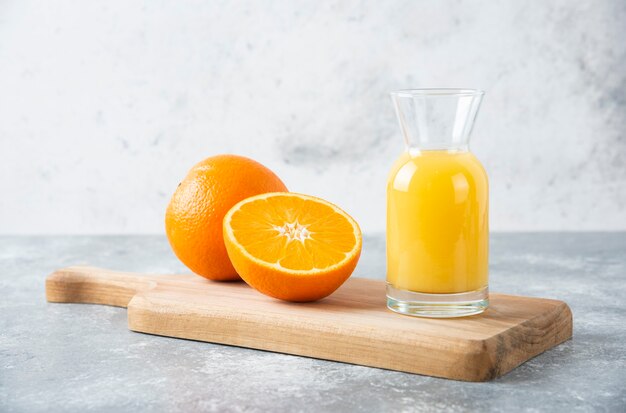 Jarra de vidrio de jugo con rodajas de naranja sobre una tabla de madera.