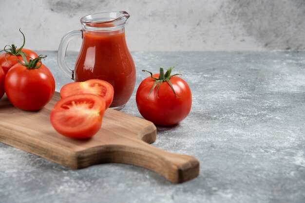 Una jarra de vidrio de jugo con tomates frescos.