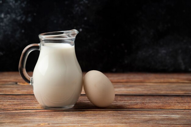 Jarra de vidrio de leche y huevo sobre mesa de madera.