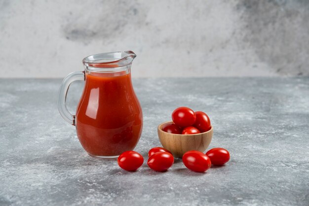 Una jarra de vidrio llena de jugo de tomate con un cuenco de madera de tomate cherry.
