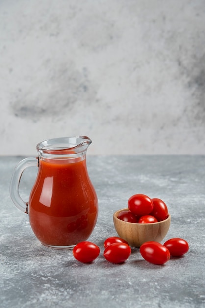 Una jarra de vidrio llena de jugo de tomate con un cuenco de madera de tomate cherry.