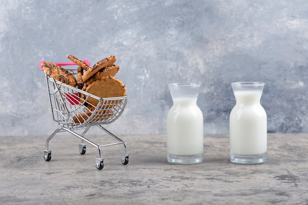 Jarras de vidrio de leche fresca con deliciosas galletas colocadas sobre una mesa de mármol.