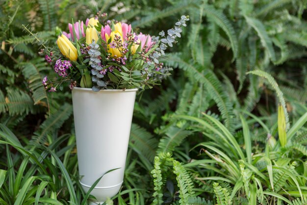 Jarrón con flores de colores y vegetación de fondo