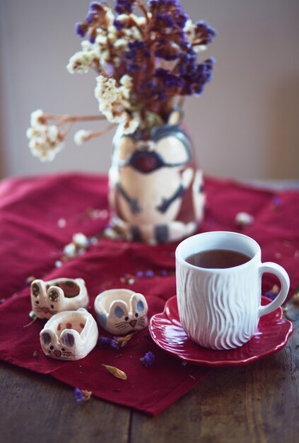 El jarrón con flores, taza, mandarina y battledore se paran en la mesa