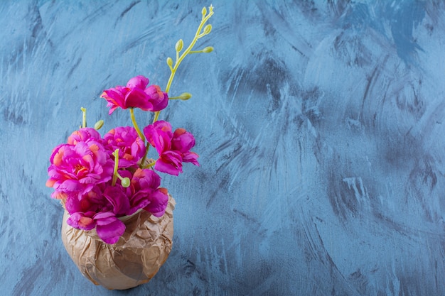 Un jarrón de papel con hermosas flores frescas de color púrpura sobre azul.