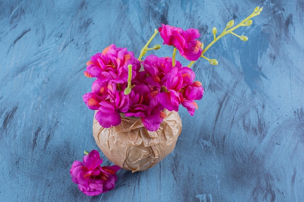 Un jarrón de papel con hermosas flores frescas de color púrpura sobre azul.