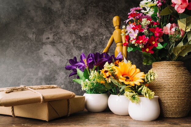 Jarrones de flores con figuras de madera simuladas y cajas de regalo en mesa de madera