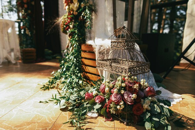 Jaula de pájaros decorativa llena de rosas rojas, spearworts y vegetación