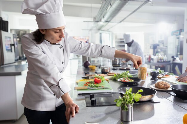 La jefa de cocina mujer añadiendo hierbas para completar un plato gourmet en una cocina moderna
