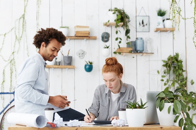 Jefe diseñador masculino de piel oscura sentado en la mesa con smartphone