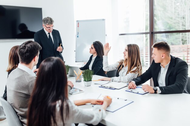 Jefe empresario sosteniendo papeles manos y sonriendo. Joven equipo de compañeros de trabajo haciendo gran discusión de negocios en la oficina moderna de coworking.