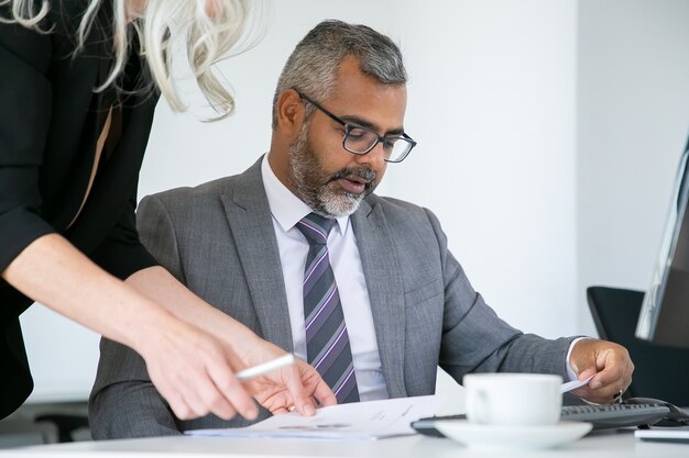 Jefe enfocado analizando el informe de los gerentes, leyendo y revisando documentos mientras está sentado en el lugar de trabajo. Concepto de comunicación empresarial