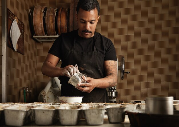 El jefe del hombre negro está preparando moldes para pasteles antes de llenarlos con masa en su confitería artesanal profesional