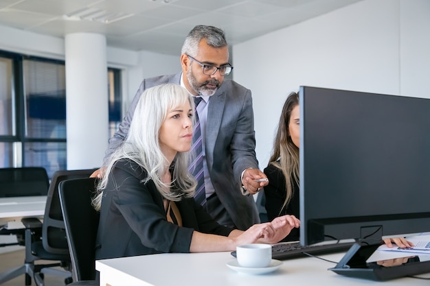 Jefe mirando y apuntando al monitor, comentando el proyecto mientras el gerente escribe y trabaja en la presentación. Tiro medio. Concepto de comunicación empresarial