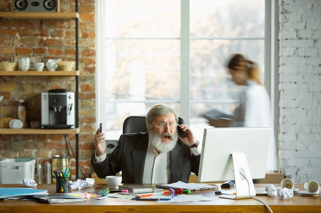 Foto gratuita jefe nervioso y cansado en su lugar de trabajo ocupado mientras la gente moviéndose cerca borrosa. trabajador de oficina, gerente trabajando, tiene problemas y fecha límite, sus colegas distraen. negocio, trabajo, concepto de carga de trabajo.