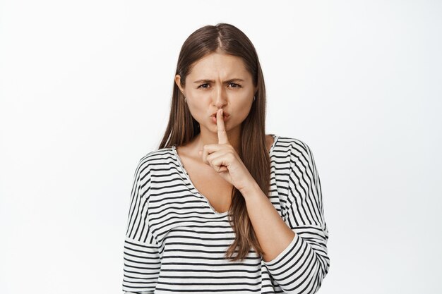 Jefe de niña enojada callando, haciendo el gesto de silencio, presione el dedo en los labios en un gesto tabú, diciendo que se quede callado en blanco