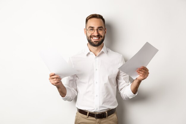 Jefe satisfecho sonriendo mientras sostiene un buen informe, leyendo documentos, de pie