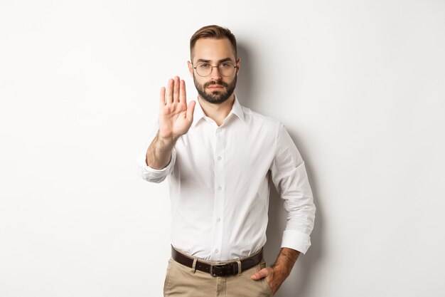 Jefe serio con gafas mostrando señal de stop, diciendo que no, prohibiendo algo, de pie blanco