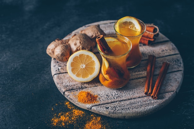 Jengibre en polvo en tazas de té con limón, jengibre y canela seca Vista de ángulo alto sobre madera sobre un fondo oscuro con textura