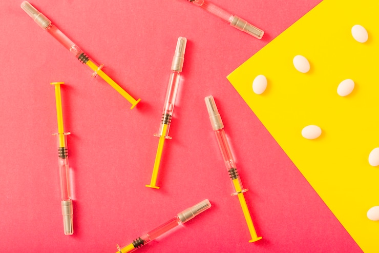 Foto gratuito jeringa y pastillas blancas sobre fondo rojo y amarillo