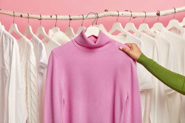 Foto gratuita jersey casual morado en perchas en mano de mujer contra riel con ropa blanca como la nieve.