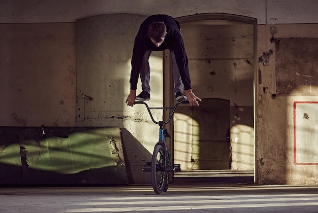 Jinete de BMX haciendo acrobacias con una bicicleta en un lugar en cuclillas.