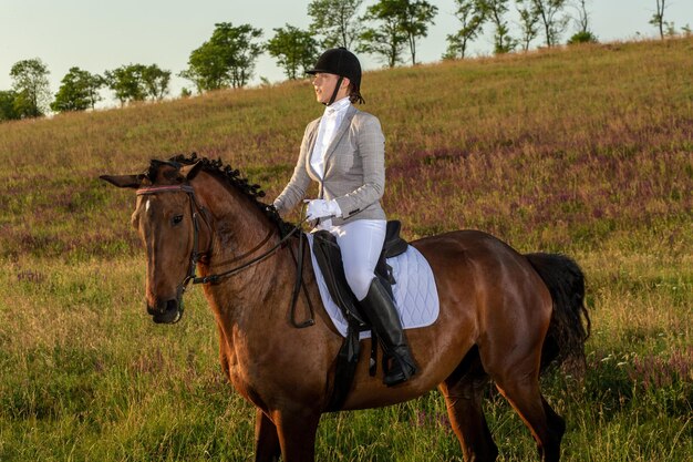 Jinete de la mujer joven con su caballo en la luz del atardecer por la noche. Fotografía al aire libre en el estado de ánimo de estilo de vida.