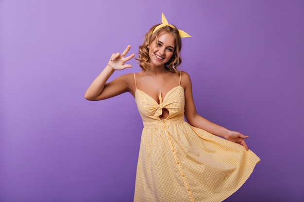 Jocund joven europea divirtiéndose durante la sesión de retratos de moda de verano. Retrato de niña rizada increíble en traje amarillo.