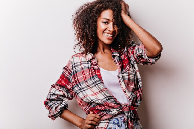 Jocund mujer joven en camisa roja de pie en pose de confianza. alegre chica morena aislada en blanco.