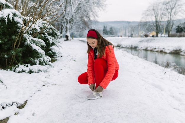 Foto gratuita jogger mujer atar cordones de los zapatos cerca del lago en invierno