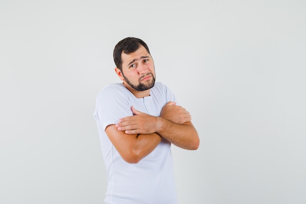 Joven abrazándose a sí mismo en camiseta y con frío. vista frontal.