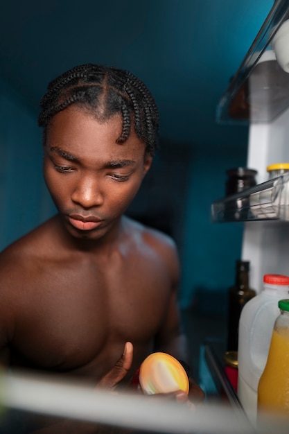 Joven abriendo la nevera en casa para tomar un refrigerio en medio de la noche