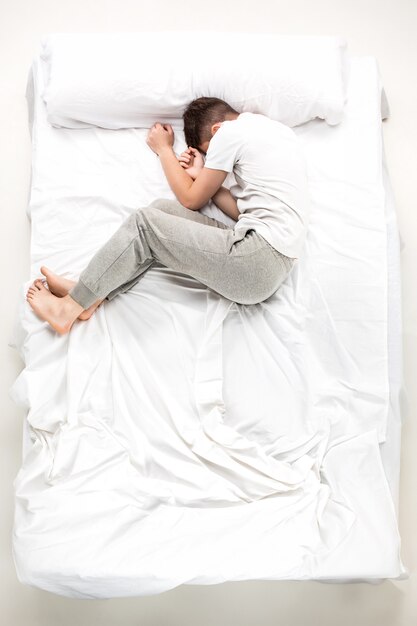 El joven acostado en una cama blanca, vista superior