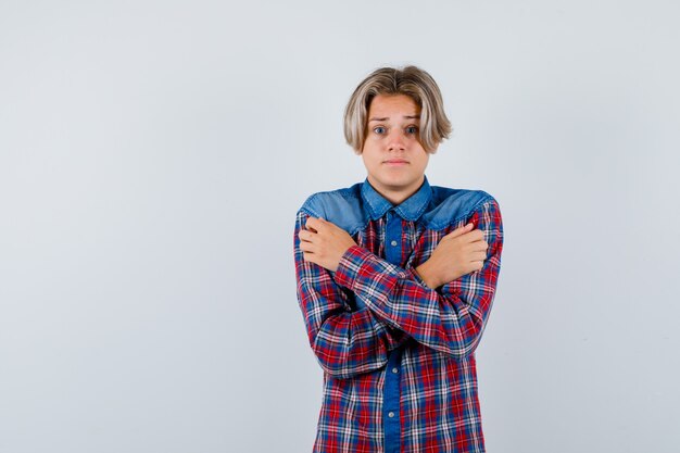 Joven adolescente abrazándose a sí mismo, sintiendo frío en camisa a cuadros y luciendo indefenso. vista frontal.