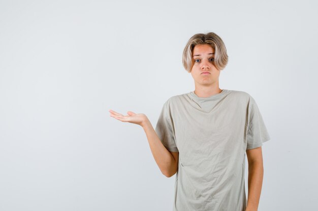 Joven adolescente en camiseta extendiendo la palma a un lado y mirando confundido