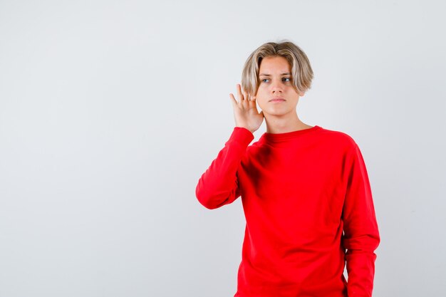 Joven adolescente escuchando una conversación privada en suéter rojo y mirando confundido. vista frontal.