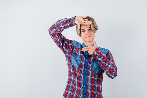 Joven adolescente haciendo gesto de marco en camisa a cuadros y mirando alegre