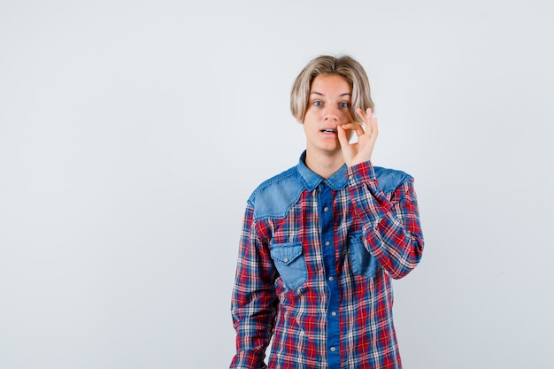 Foto gratuita joven adolescente mostrando gesto de cremallera en camisa a cuadros y mirando con cuidado