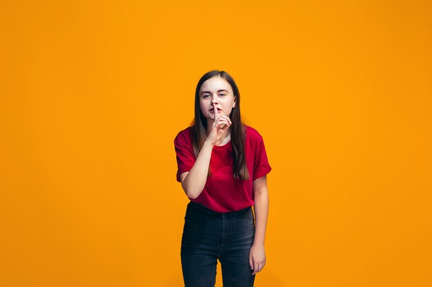La joven adolescente susurrando un secreto detrás de su mano sobre la pared naranja