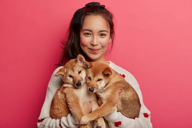 Joven adora a los perros, juega con dos cachorros shiba inu, les enseña a realizar algunas acciones, ha adoptado lindos animales, yendo al veterinario, aislado sobre fondo rosa.