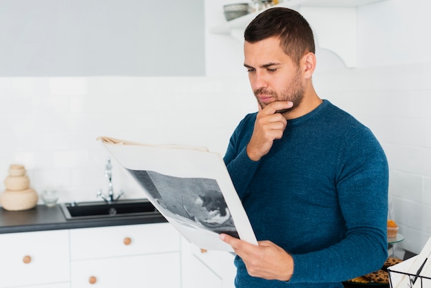 Joven adulto está leyendo el periódico en la cocina