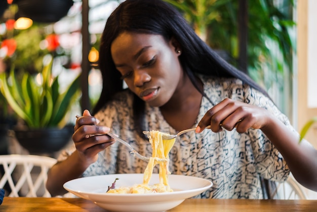 Joven africana comiendo espaguetis en restaurante.